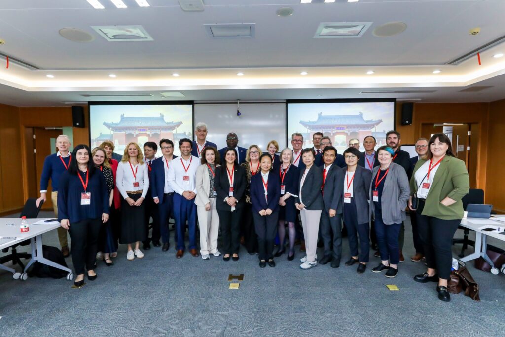 Grupo de participantes en una reunión internacional con fondo de presentación.