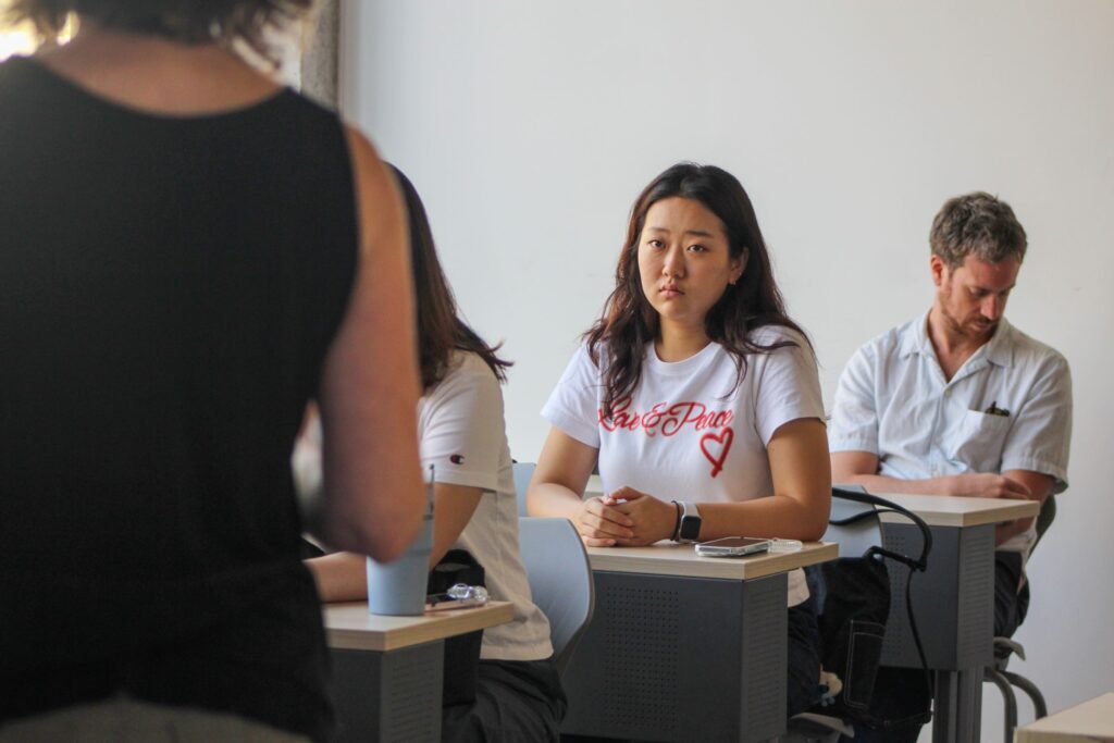 Mujer joven con camiseta blanca, mirando al frente en clase.