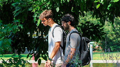 Dos estudiantes caminando por un jardín del campus San Joaquín de la Pontificia Universidad Católica de Chile.